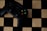 A black gaming controller with colorful buttons labeled X, Y, A, and B is placed on a wooden chessboard.
