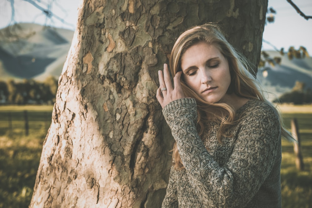 woman in black and gray long sleeve shirt leaning on brown rock during daytime