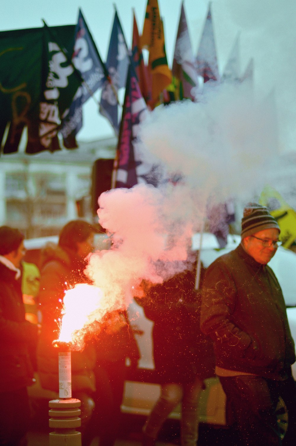 Hombre en chaqueta marrón sosteniendo humo rojo y blanco