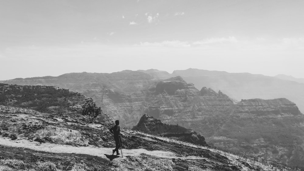 grayscale photo of man walking on rocky mountain