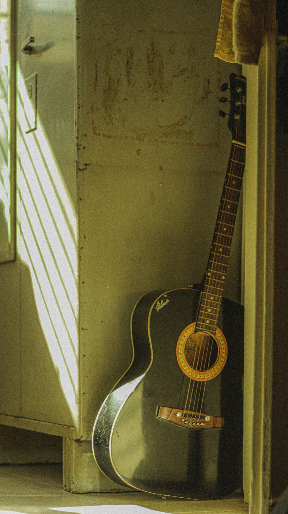 black acoustic guitar leaning on white wall