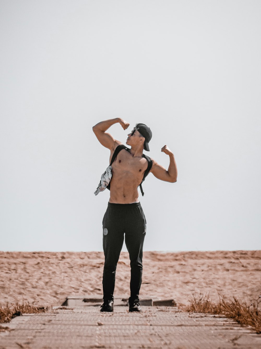 man in black pants and black tank top standing on brown sand during daytime