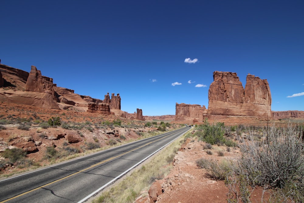 brown rock formation near gray asphalt road under blue sky during daytime