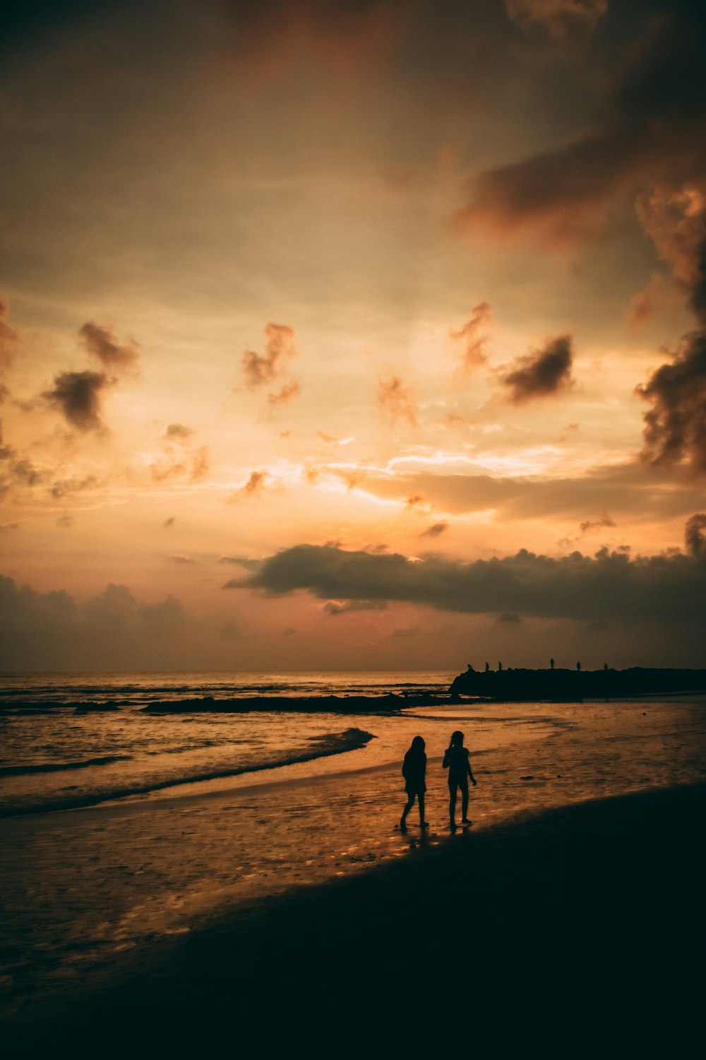 silhouette of 2 people walking on beach during sunset