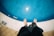 A pair of bare feet stands at the edge of a swimming pool. The water is clear and blue, with sunlight reflecting off the surface, creating a sparkling effect. The pool's depth is marked as 1.30 meters on a sign on the edge.