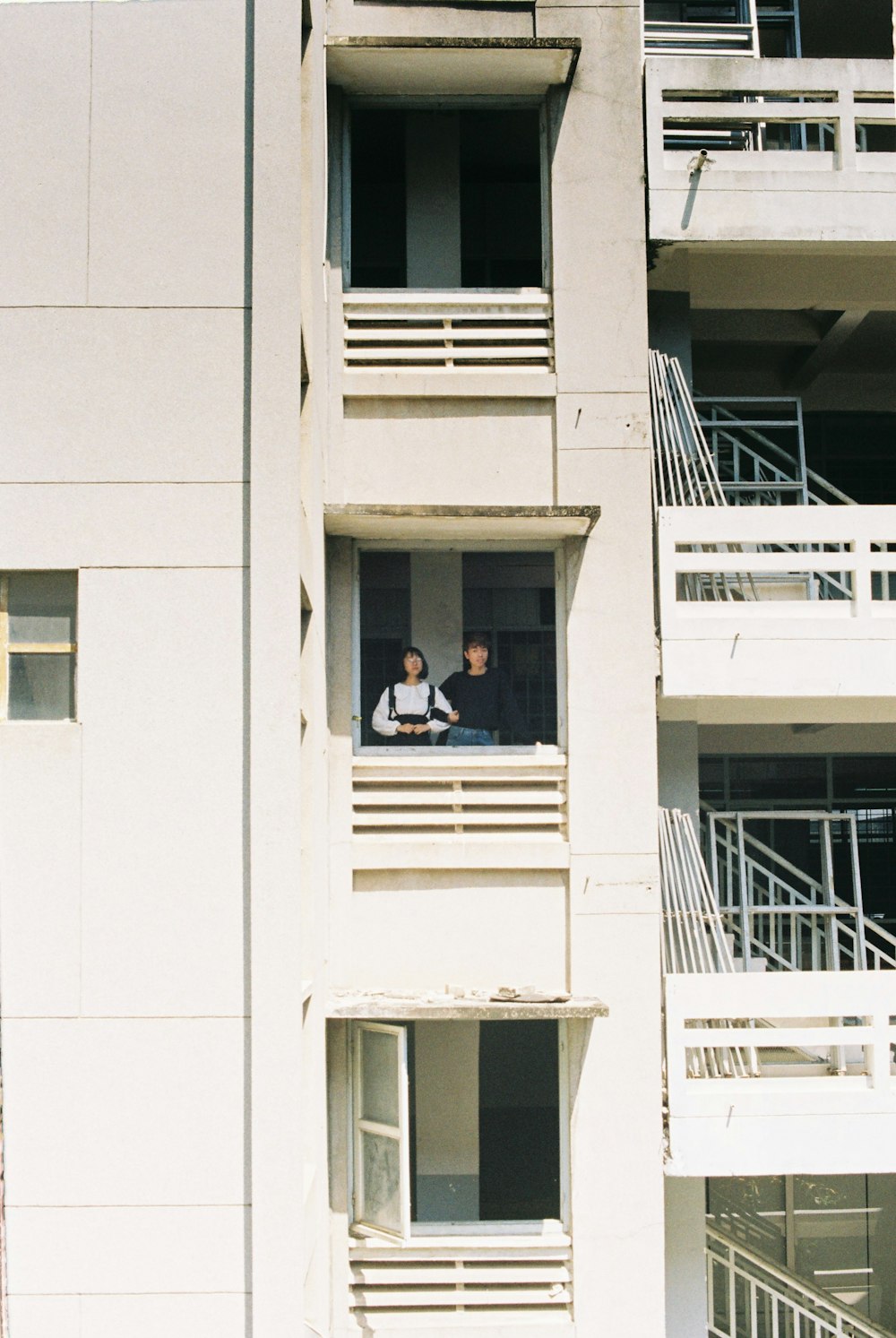 man in white shirt sitting on white concrete window during daytime