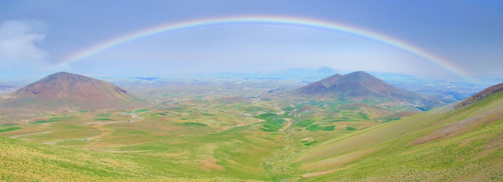 green mountains under rainbow and white clouds during daytime