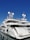 A luxurious white yacht docked at the marina under a clear blue sky. The yacht features multiple decks, satellite antennas, and is securely tied to the dock.