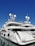 A luxurious white yacht docked at the marina under a clear blue sky. The yacht features multiple decks, satellite antennas, and is securely tied to the dock.