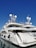 A luxurious white yacht docked at the marina under a clear blue sky. The yacht features multiple decks, satellite antennas, and is securely tied to the dock.