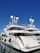 A luxurious white yacht docked at the marina under a clear blue sky. The yacht features multiple decks, satellite antennas, and is securely tied to the dock.