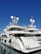 A luxurious white yacht docked at the marina under a clear blue sky. The yacht features multiple decks, satellite antennas, and is securely tied to the dock.