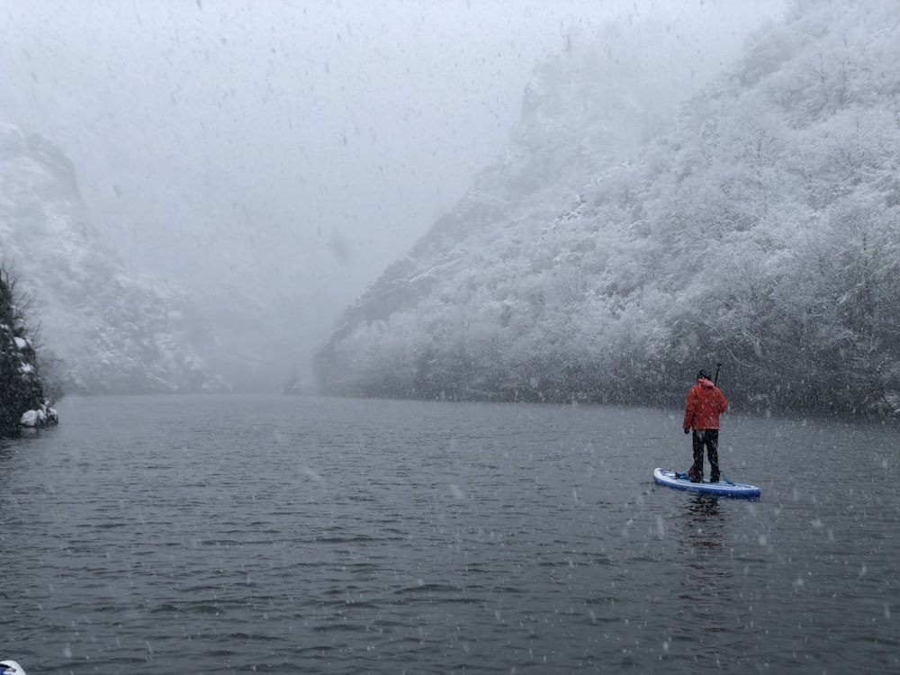 person in red jacket riding blue kayak on body of water during daytime