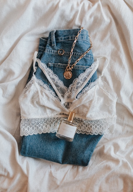 A casual outfit laid out flat: denim jeans, a white blouse, and a light scarf