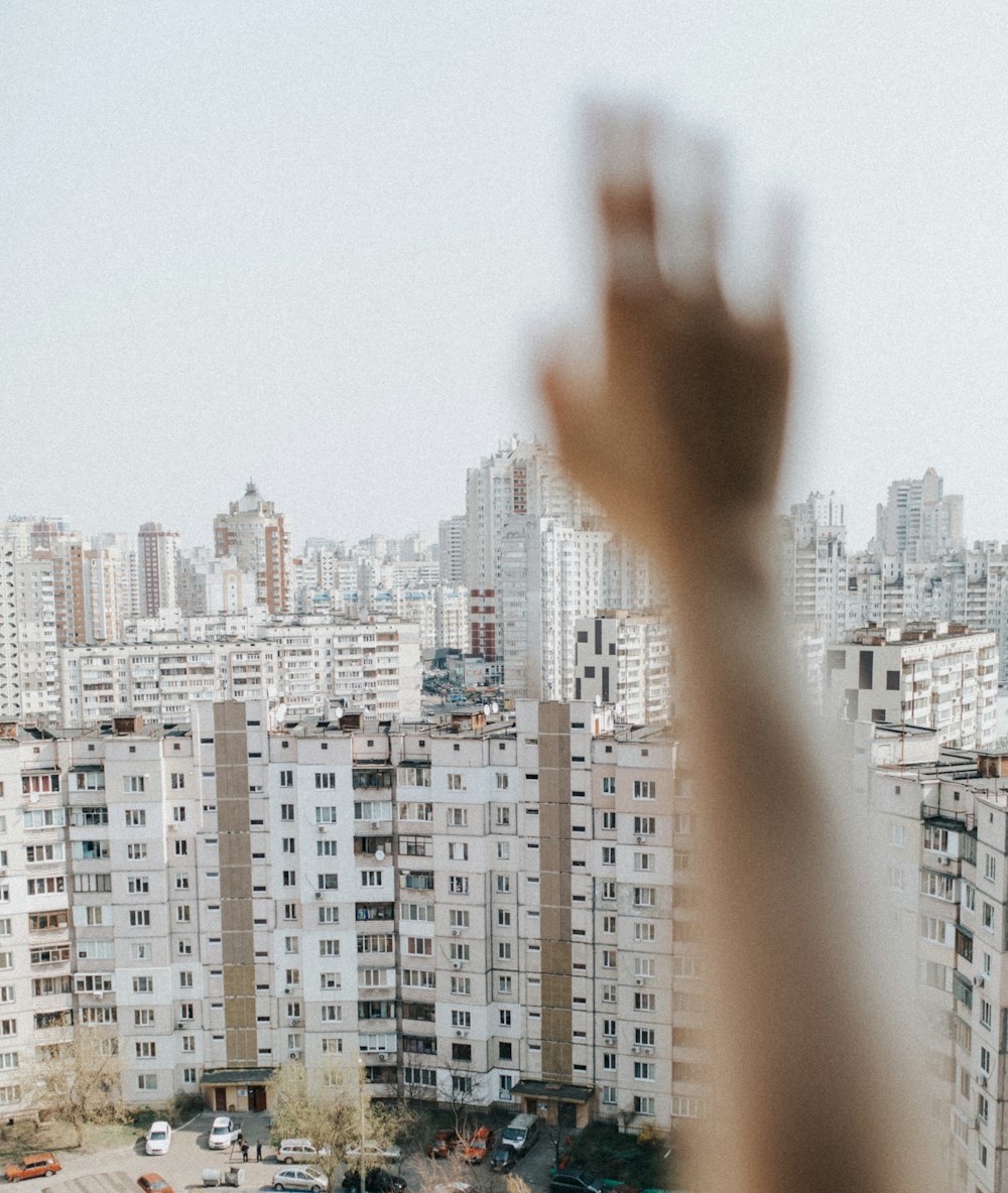 person raising hand in front of white concrete building during daytime