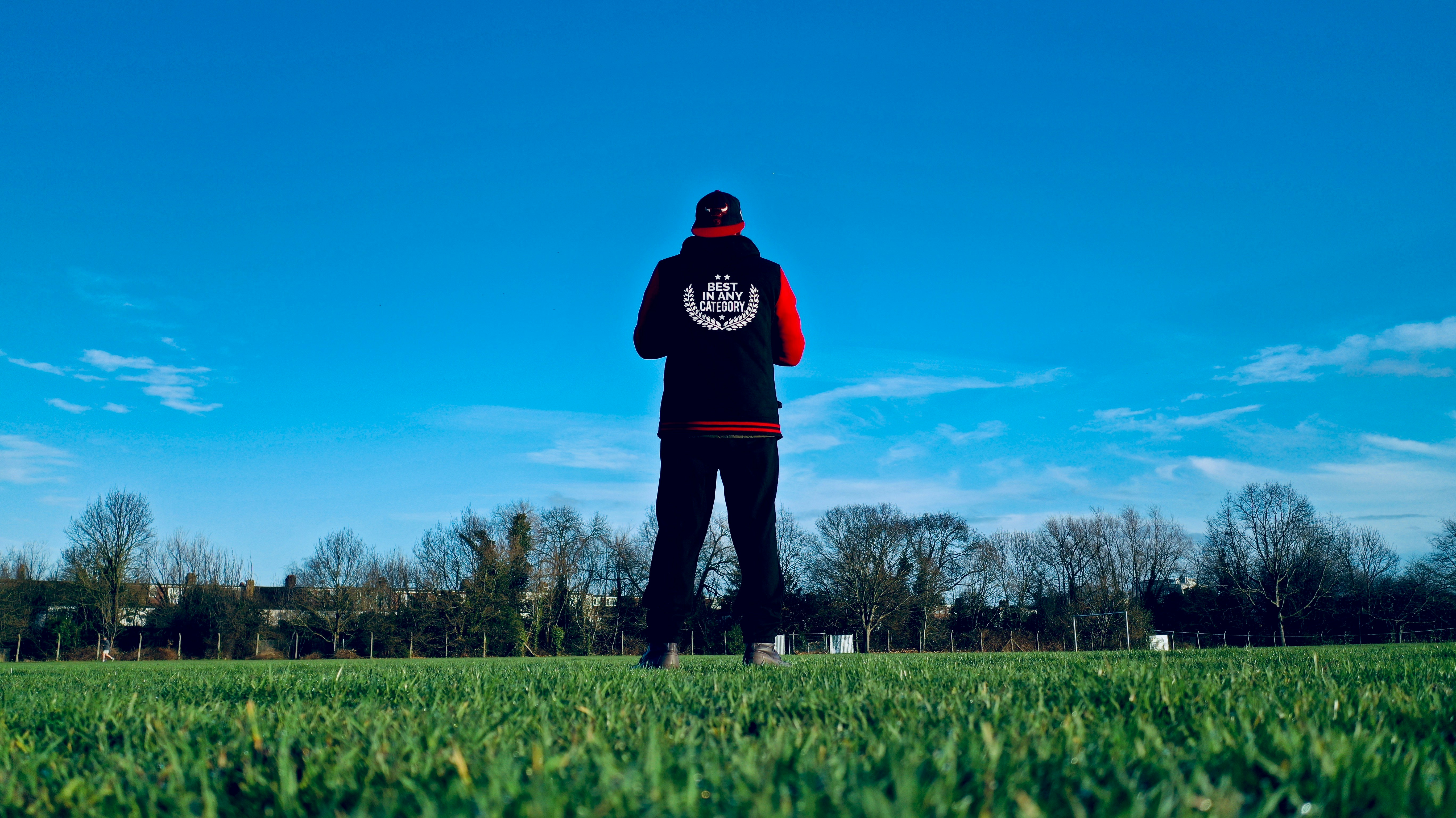 man in black hoodie standing on green grass field under blue sky during daytime