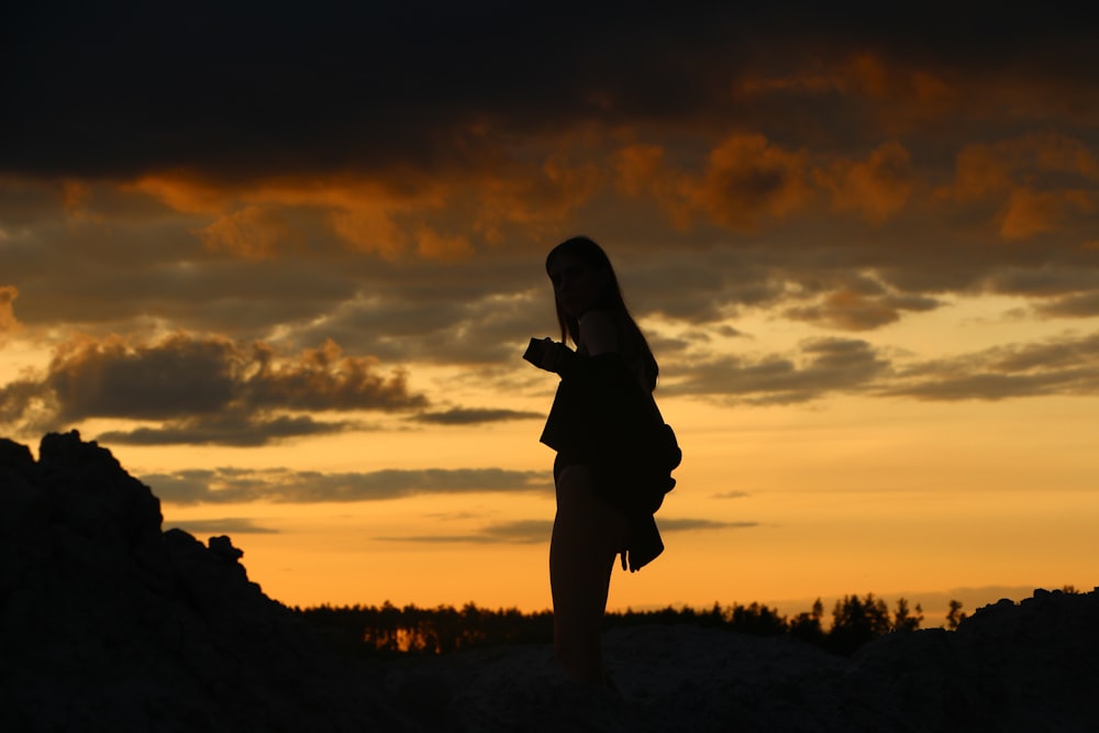 silhouette of woman standing on grass field during sunset