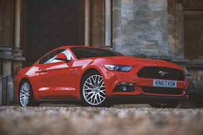 Red luxury coupe with polished rims parked in front of a modern glass building