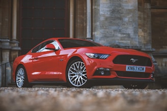 Red luxury coupe with polished rims parked in front of a modern glass building