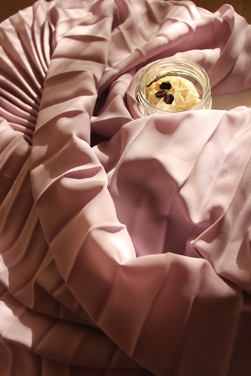 Close-up of a silky smooth satin sleep bonnet in soft blush pink draped elegantly on a vintage wooden chair.