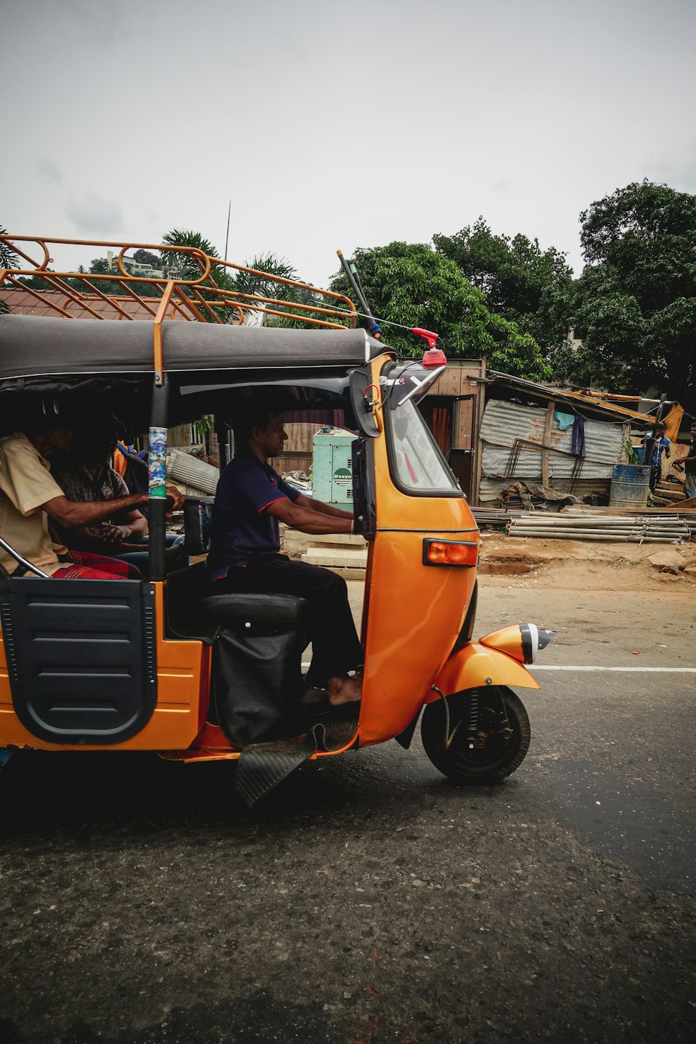 man in black t-shirt driving orange and black auto rickshaw