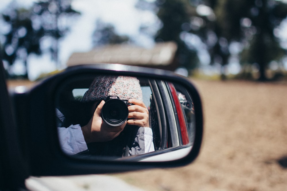 Persona che indossa occhiali da sole neri che scatta foto dello specchietto laterale dell'auto