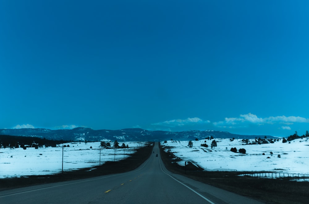 gray concrete road near snow covered field under blue sky during daytime