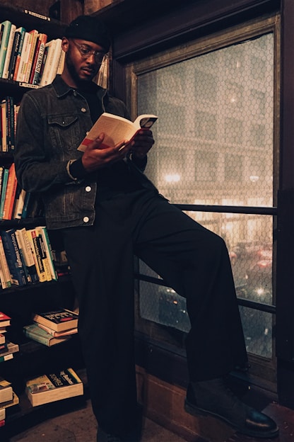A thoughtful man reading a book in a cozy library setting.
