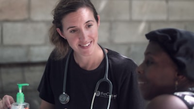 woman in black crew neck shirt wearing blue earbuds nurse google meet background