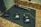Several Sennheiser wireless microphone transmitters and receivers are laid out on a black mat on a countertop. There is also a handheld microphone positioned next to them. The devices appear to have display screens and numbered labels.