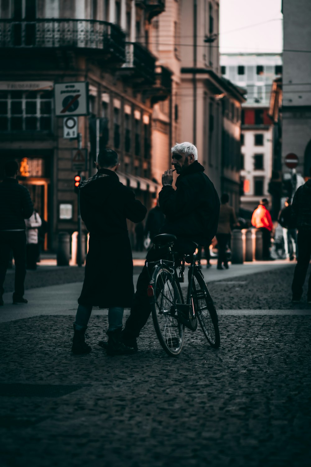 man in black jacket and black pants standing beside black bicycle during daytime