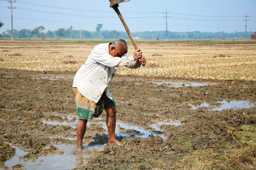 man in white shirt and green shorts holding brown wooden stick during daytime