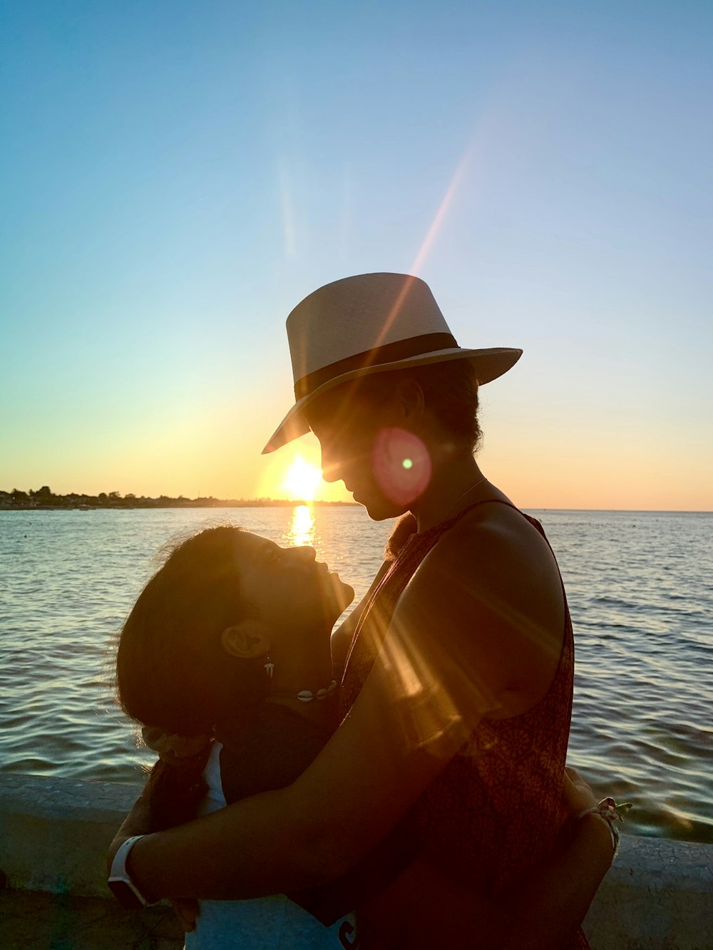 silhouette of woman wearing hat near body of water during sunset