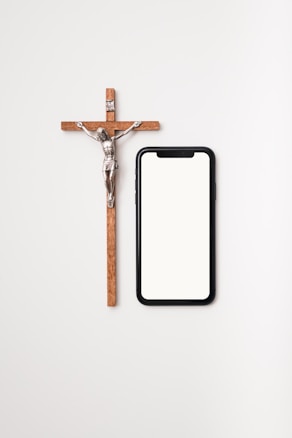 A wooden crucifix with a metal figure next to a modern smartphone with a blank screen on a light background.
