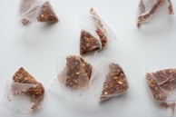Several triangular tea bags filled with loose leaf tea containing various dried ingredients. The tea bags are translucent, allowing the different textures and colors of the tea to be visible. They are spread out on a plain white surface.