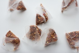 Several triangular tea bags filled with loose leaf tea containing various dried ingredients. The tea bags are translucent, allowing the different textures and colors of the tea to be visible. They are spread out on a plain white surface.