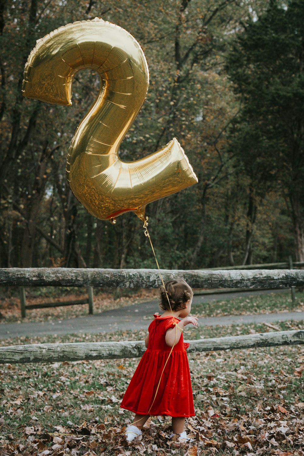 girl in red dress holding gold heart shaped balloon