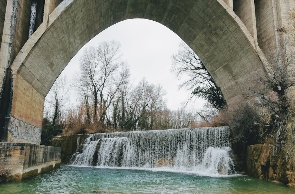 water falls under white arch bridge