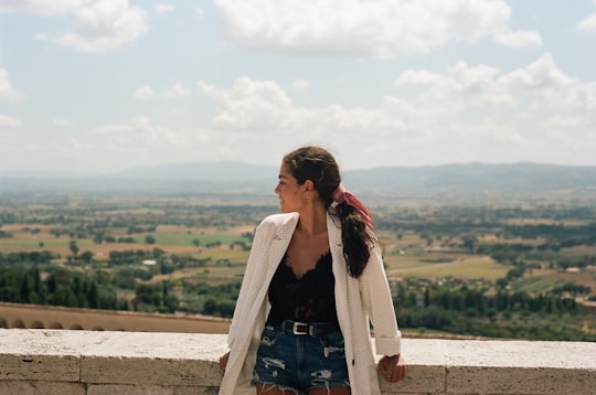 woman in gray cardigan standing on brown field during daytime in Assisi Italy