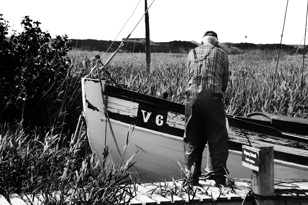 man in plaid shirt and pants standing on boat in grayscale photography