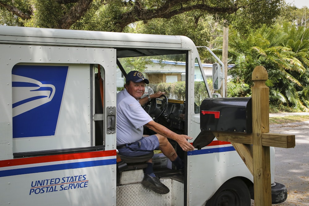 man in blue dress shirt sitting on white and blue bus during daytime