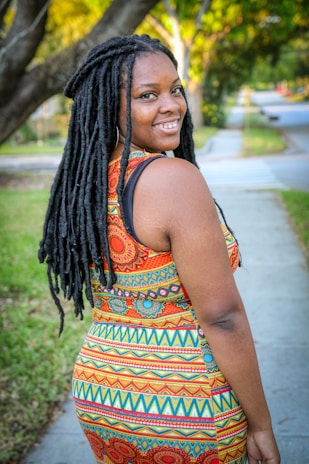 A smiling customer wearing a flowing eco-friendly dress in a green outdoor setting.