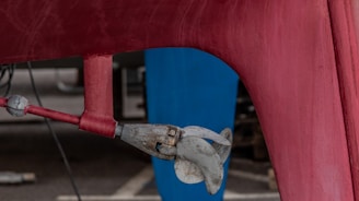 A close-up view of a boat propeller attached to the bottom of a red hull. The propeller is metallic and appears slightly weathered. The background includes a blue vertical structure and a concrete surface.