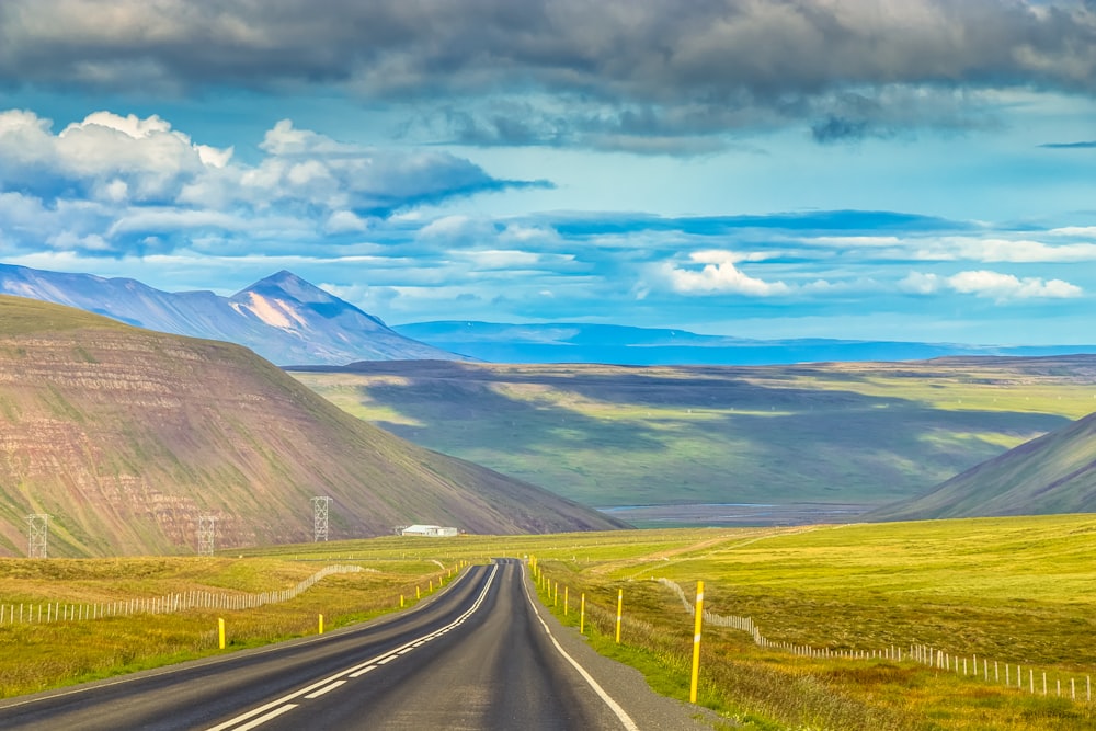 gray asphalt road near green grass field under blue sky during daytime