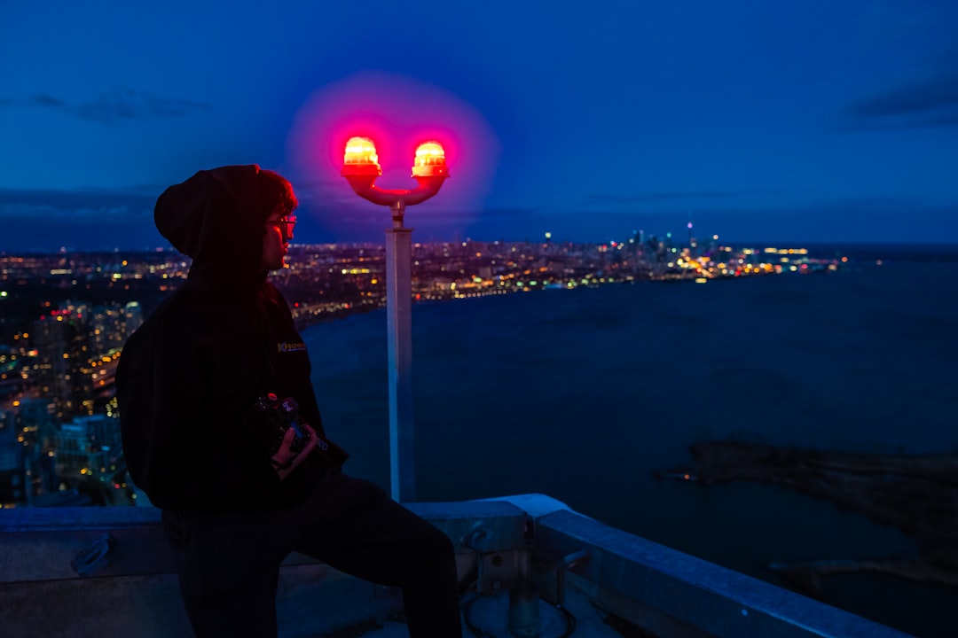 person in black hoodie standing on top of building looking at the city lights during night