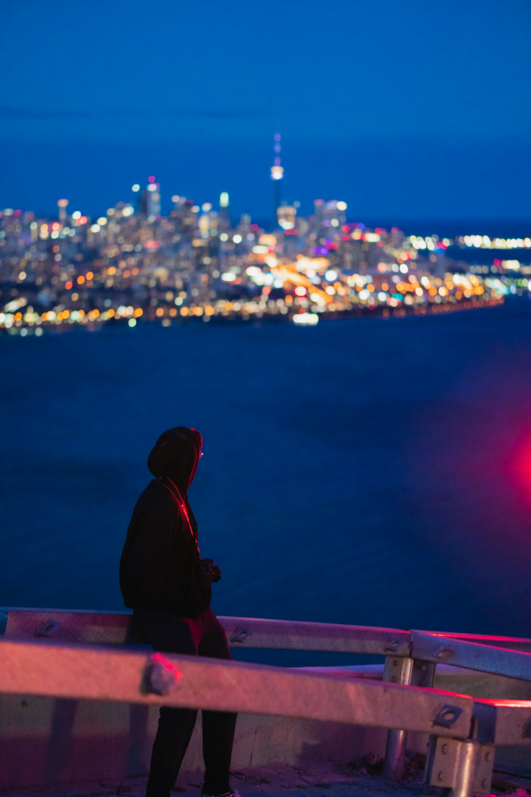 man in black hoodie sitting on brown wooden bench looking at city lights during night time