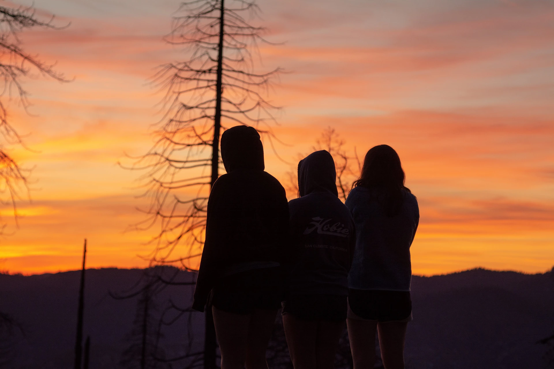 silhouette of 3 people standing on mountain during sunset