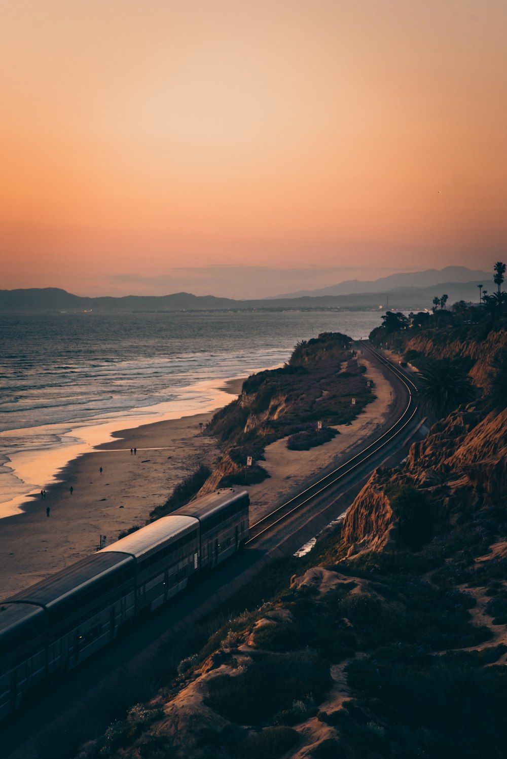 trem branco e preto no trilho perto do corpo de água durante o pôr do sol