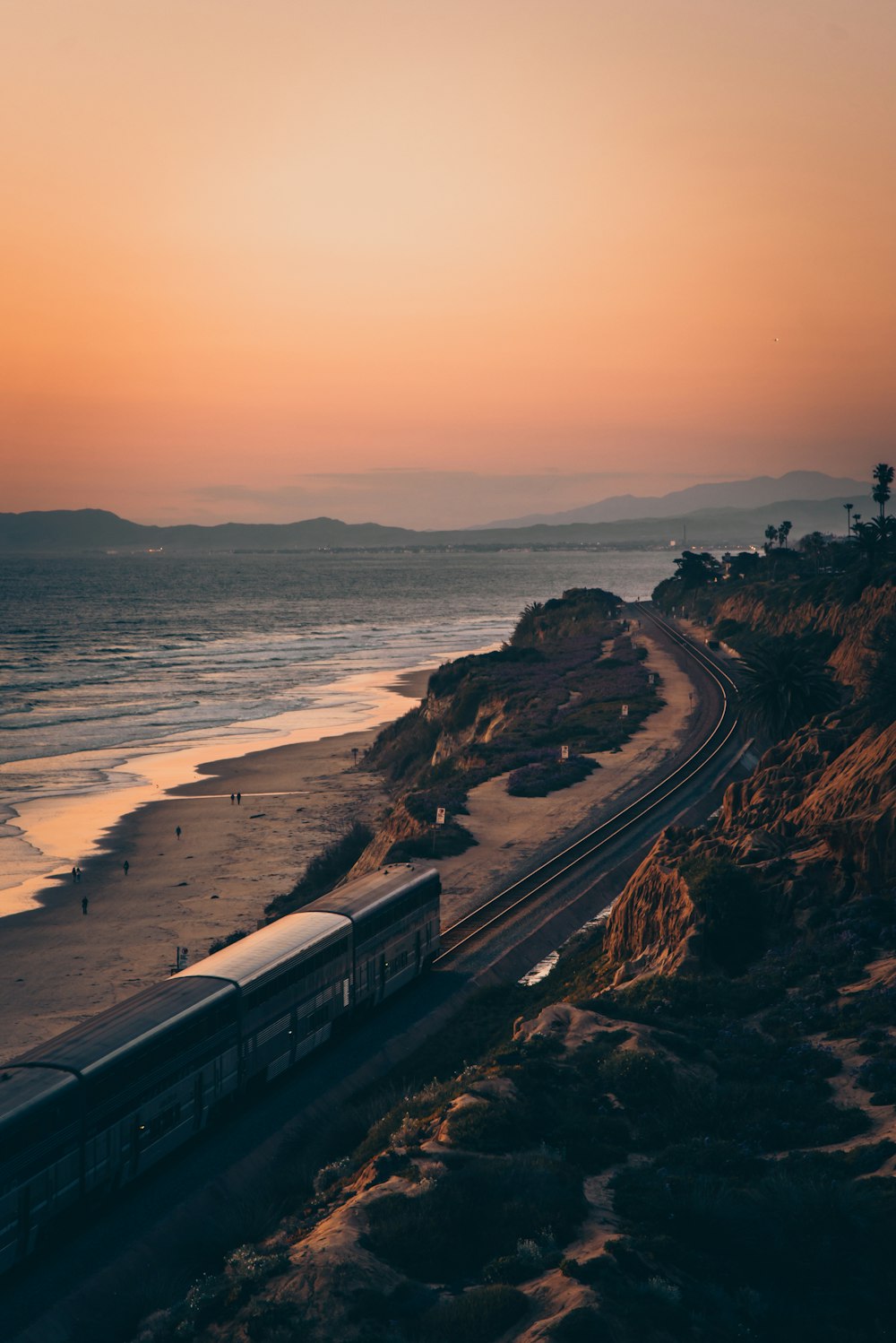 white and black train on rail near body of water during sunset