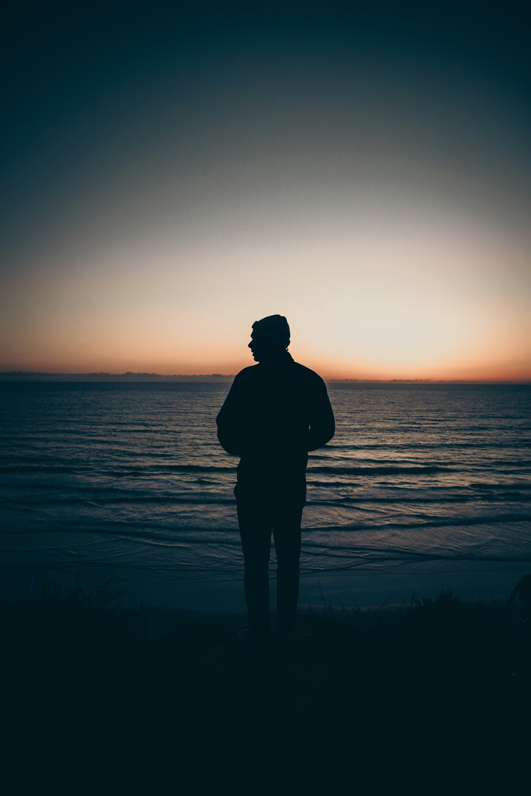 silhouette of man standing near body of water during sunset